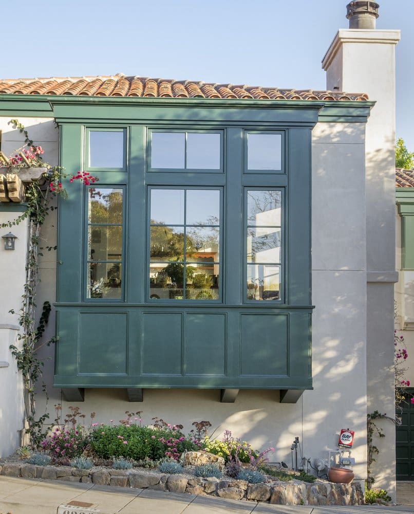 A green window with shutters on the outside of a house.