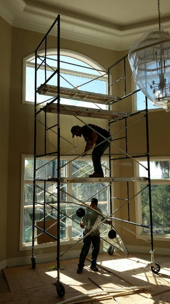 A man standing on top of scaffolding in front of windows.